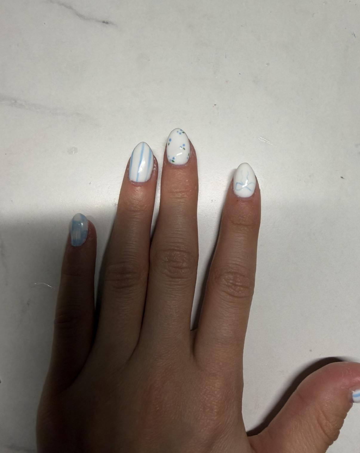 Custom white and blue gel nail art with delicate lines and tiny floral details by Raegan